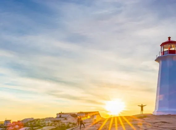 Visitors pose under the Peggy's Cove Lighthouse at dusk