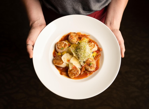 A pair of hands holding a colourful scallop dish