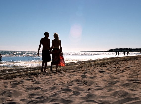 Two silhouetted figures walk along Parlee Beach