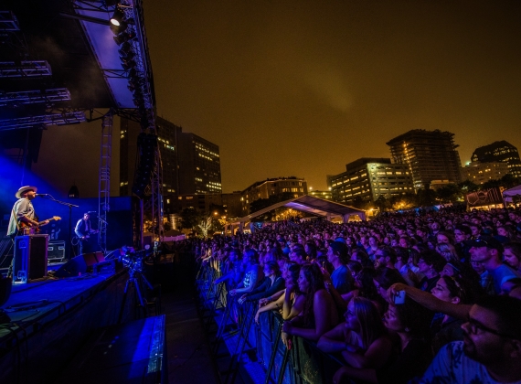 A musician performs to a large crowd on the Halifax water front at night.