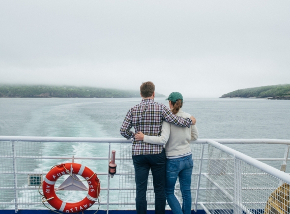 A couple, arm in arm, looking out off the stern of the ferry