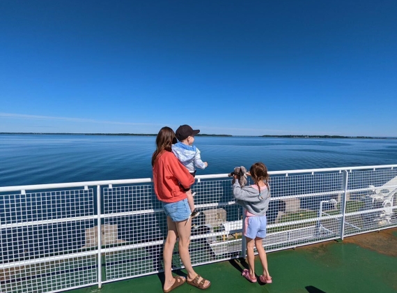 A young family stands near the railing of the ferry, looking out on the ocean