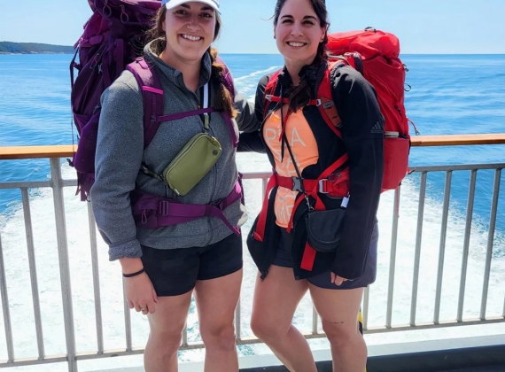 Two backpackers stand against the rail of the ferry