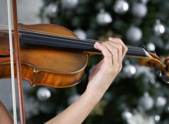 Hand of a female violinist on the fingerboard of a violin with Christmas tree - stock photo