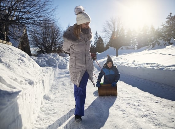 Mother pulling son on toboggan on a sunny winter day - stock photo