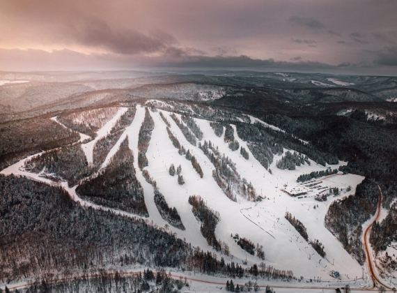 Arial view of ski slopes on a snowy mountain on a cloudy day with some sun shining through.