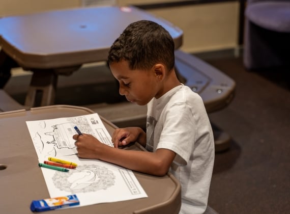 A boy seated, colouring with crayons