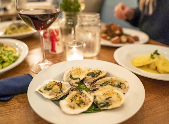 A plate of oysters on a candle lit table with other dishes in the background.