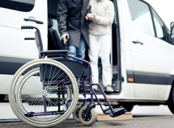 A person assistance another person with mobility issues out of a shuttle and into a wheelchair