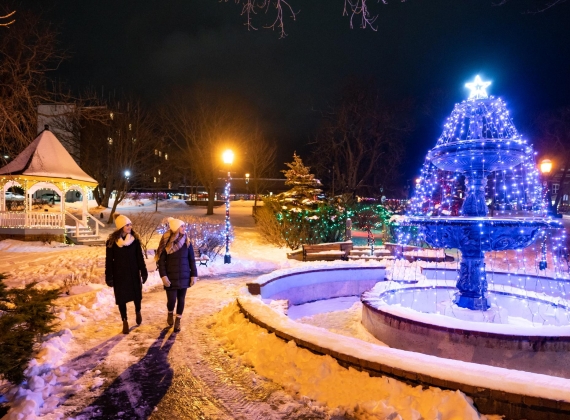 Two people walking around a snowy, lit up park at night.