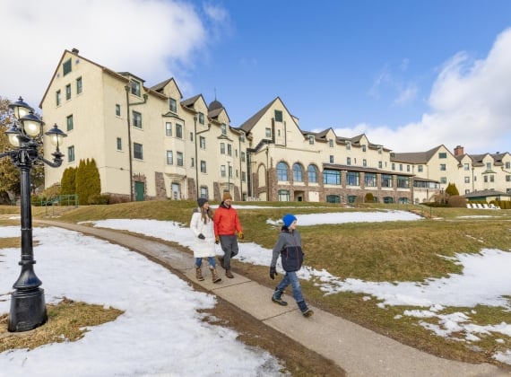 A family walking down a path outside of a grand building on a snowy, sunny day.