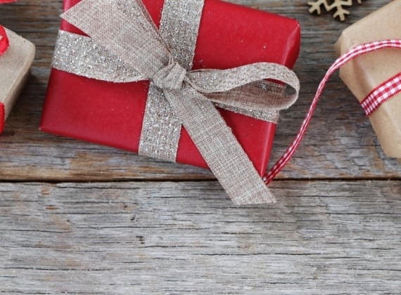 3 gifts wrapped in red and brown wrapping paper on a wooden back drop with fir branches and snowflake decorations.