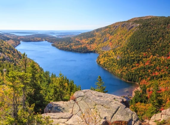 Looking down at a large pond in a lush green and red valley from a cliff on a sunny day.