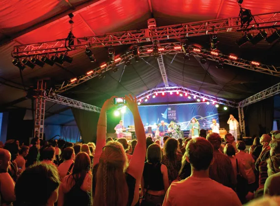 View from the crowd of a band playing music on a tented stage.