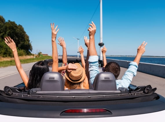 A group joyously throwing their hands up in the air while riding in a convertible