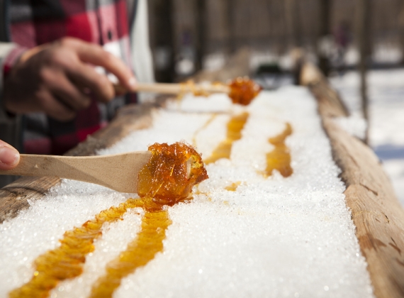 A wooden spoon runs along maple sugar and snow at a sugar shack