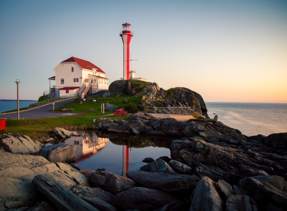 A lighthouse and building on a rocky sea side cliff at sunset.