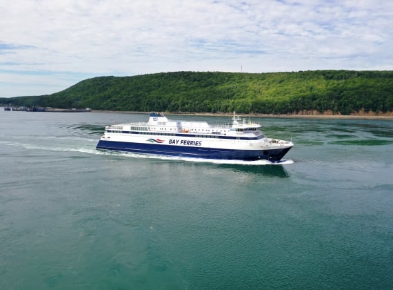 A ferry sailing in calm waters with lush green hills in the background.