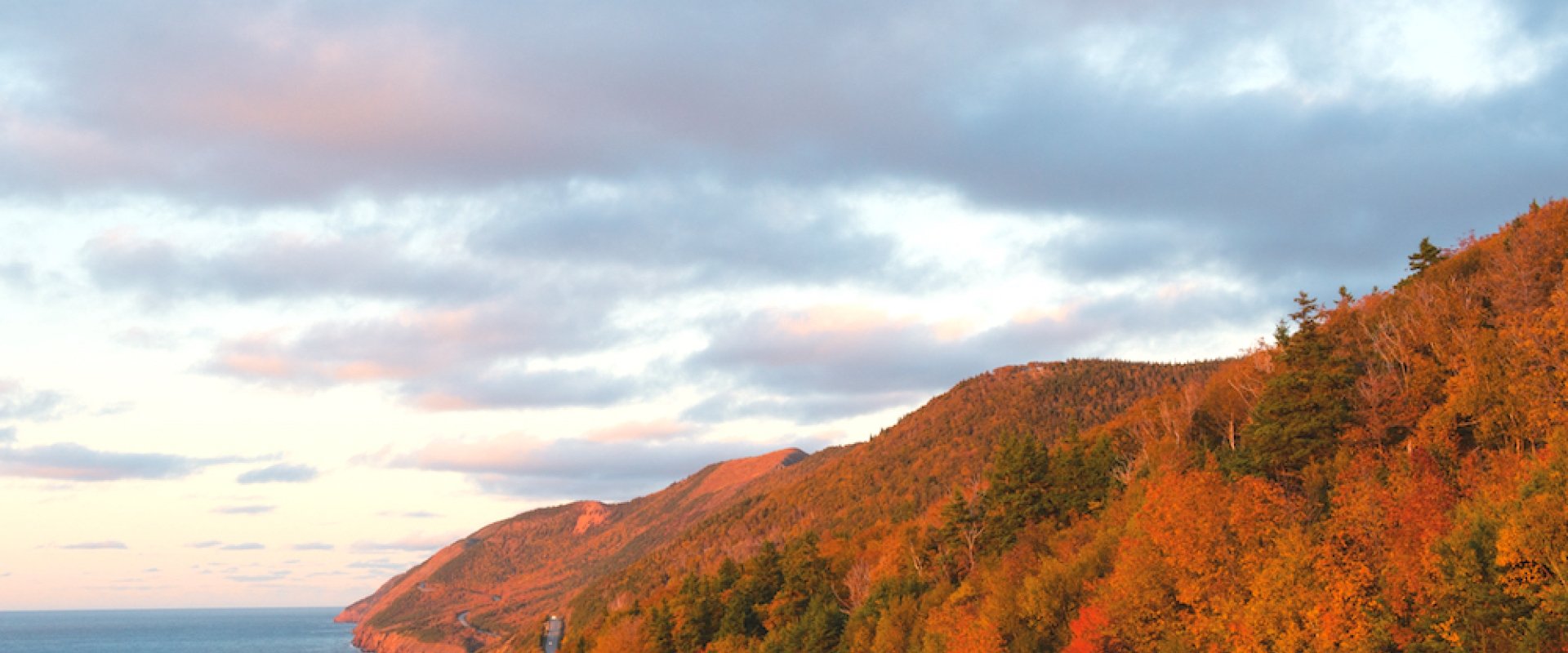 The winding road of the Cabot Trail, at the base of the red-tree lined mountains in fall