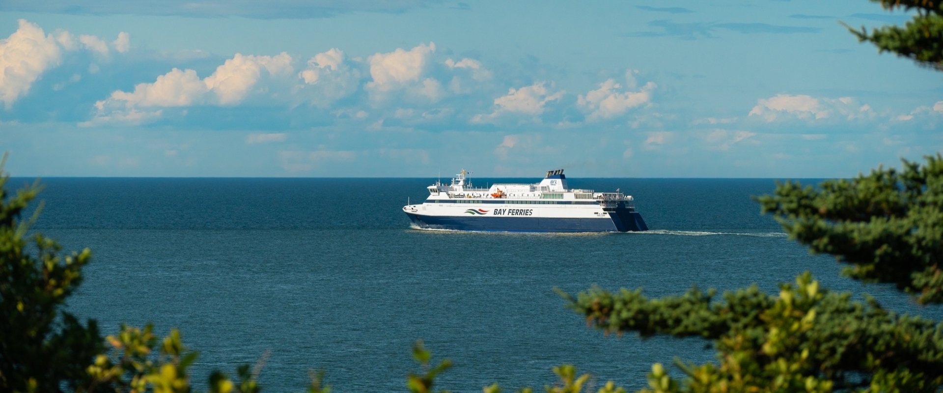 A large ferry sailing in the ocean from a distance on a sunny day, blue skies with a few clouds.