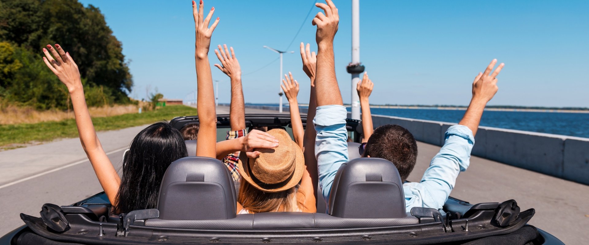 A group joyously throwing their hands up in the air while riding in a convertible