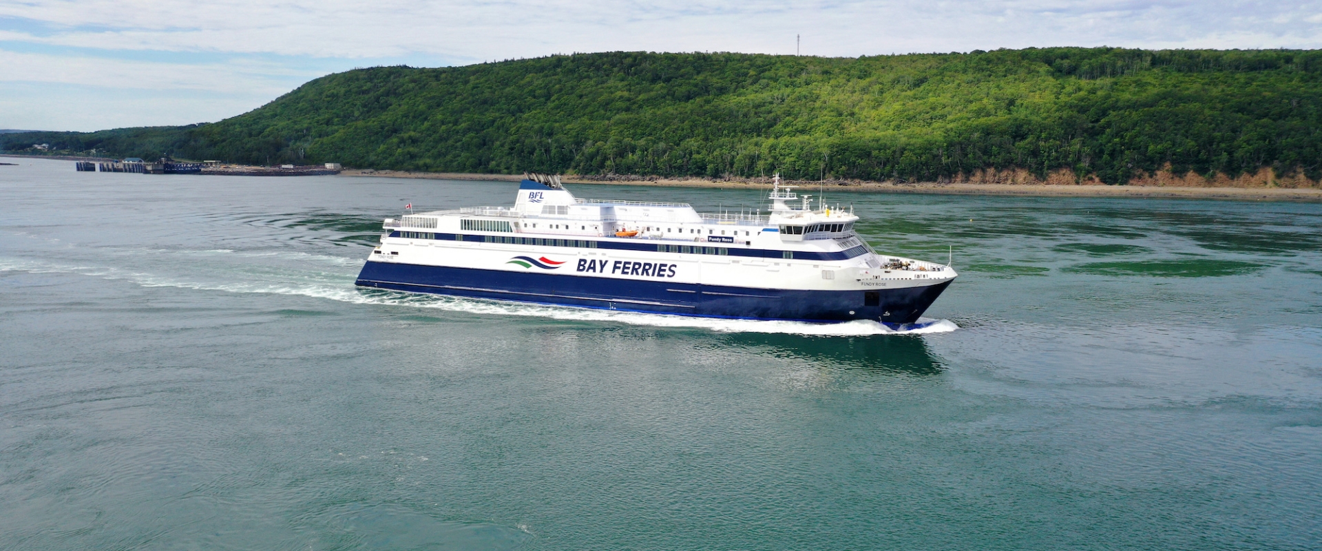 A ferry sailing in calm waters with lush green hills in the background.
